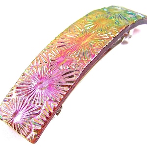 May include: A iridescent pink and gold glass hair clip with a floral design.