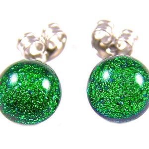 May include: A pair of stud earrings with a round, green, speckled design. The earrings have a silver-colored backing. The green color has a glittery effect. The earrings are set against a white background.