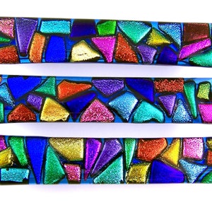 Peut inclure: Trois tirettes de tiroir en verre coloré avec un motif en mosaïque. Les tirettes sont en verre bleu, vert, violet, rouge, or et noir. Le verre est iridescent et a une surface texturée.