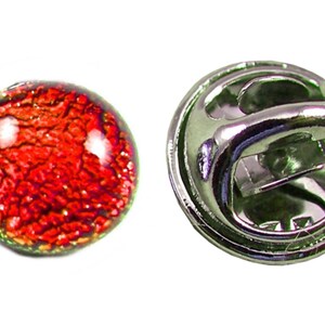 May include: A round, red and orange glass lapel pin with a textured surface. The pin has a silver-colored metal backing with a clasp.