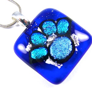 May include: A blue glass pendant with a silver and black paw print design. The pendant is attached to a silver chain.