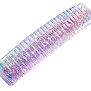 May include: A clear plastic hair clip with iridescent glitter embedded in the plastic. The clip is curved and has a rectangular shape.