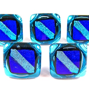 May include: Five square glass beads with a blue and silver diagonal stripe design. The beads have a dark blue square center with a lighter blue diagonal stripe. The edges are a light blue with a swirled pattern.