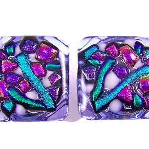 Peut inclure: Une paire de boucles d'oreilles carrées en verre avec un motif violet, blanc et iridescent. Les boucles d'oreilles présentent une mosaïque de petites pièces de verre colorées.