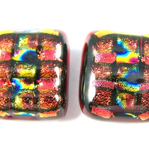 May include: Two square dichroic glass pendants. The pendants are black with a grid pattern of red and gold, and iridescent rainbow colors. The edges are red, and the background is white.