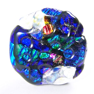May include: A dichroic glass art piece with a rounded, irregular shape. The glass features a dark blue base with iridescent accents of green, red, and silver. The surface has a textured, bubbly appearance, creating a unique, eye-catching design.