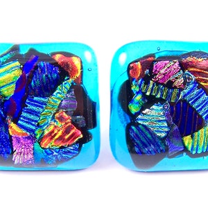 May include: A pair of square shaped earrings with a turquoise blue background and colorful iridescent glass pieces inside.