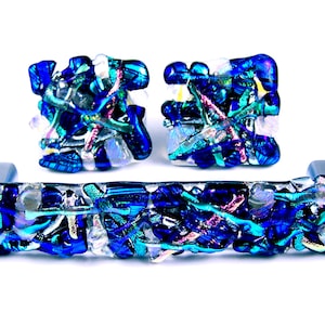 May include: A set of three blue glass cabinet knobs with a metallic iridescent finish. The knobs are made of small pieces of glass that are fused together to create a unique and textured design.