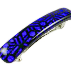 May include: A rectangular hair barrette with a blue and black geometric design. The barrette has a silver-colored metal clasp. The blue sections have a glossy finish, and the black sections appear matte.