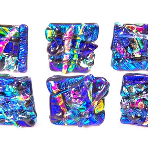 May include: Six dichroic glass squares in shades of blue, purple, and green. The glass has a textured, irregular surface, with a shimmering, iridescent quality. The squares are arranged in a grid pattern.