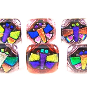 Peut inclure: Six perles carrées en verre avec un motif de papillon. Chaque perle présente un fond noir avec des morceaux de verre colorés et irisés dans les tons de bleu, vert, jaune et violet. Les perles sont transparentes sur les bords.