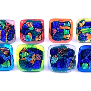 May include: Eight square glass tiles in various colours, including pink, red, orange, yellow, blue, and clear. Each tile features a mosaic of colourful, iridescent glass pieces, creating a vibrant and textured appearance. These tiles are suitable for craft projects.