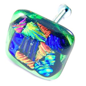 May include: A square, dichroic glass cabinet knob with a silver screw. The knob features a mix of colors, including green, blue, orange, and purple. The glass has a textured, layered appearance, and is set against a white background.
