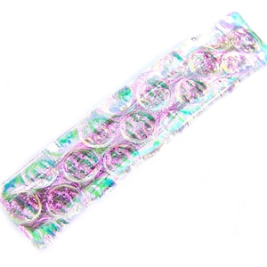 May include: Iridescent rectangular bar with a bubble-like texture. The bar has a shimmering effect with hues of pink, green, and purple. The object is set against a white background, highlighting its unique, colorful design.