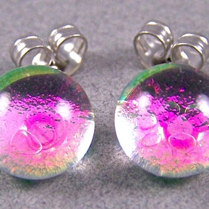 May include: A pair of iridescent pink and green glass earrings with silver posts. The earrings are round and have a textured surface.
