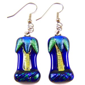May include: A pair of handcrafted earrings with a palm tree design. The earrings have a dark blue base with green and blue accents, and a gold-coloured tree trunk. The earrings are suspended from silver-coloured hooks.
