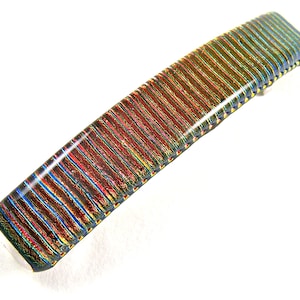 May include: A long, rectangular hair clip with a striped pattern in shades of red, blue, green, and gold. The clip has a glossy finish.