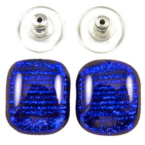 May include: A pair of square stud earrings with a dichroic glass design. The earrings feature a dark blue color with a textured, striped pattern. The earring posts are silver-colored, and the backs are clear plastic.