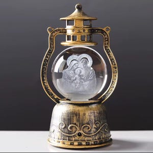 May include: An ornate lantern with a gold-coloured frame and base. A clear glass globe inside features an etched family image. The lantern has a vintage, antique appearance, with detailed decorative elements.