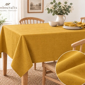 May include: A solid mustard yellow rectangular tablecloth with a visible woven texture draped over a wooden table. A circular inset shows a close-up of the fabric weave. The brand name "bohocrafts NATURAL TEXTILES" is printed in the top left corner.