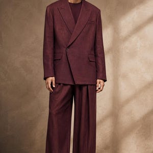 May include: A deep burgundy blazer with a single button closure and wide lapels, paired with matching wide-leg trousers. The ensemble features a textured fabric and is worn over a dark maroon shirt, completed with dark brown leather loafers.