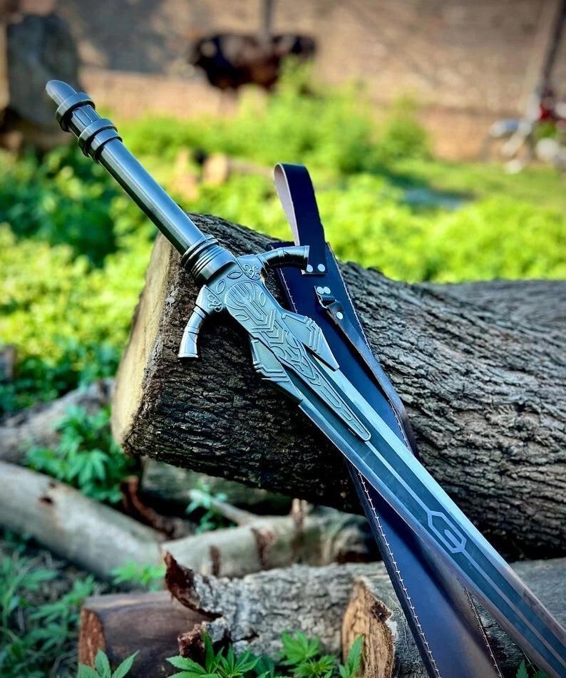 May include: A silver-colored sword with intricate designs on the hilt and blade, resting on a wooden log. The sword has a dark blue leather sheath. The background features green foliage and more wooden logs.