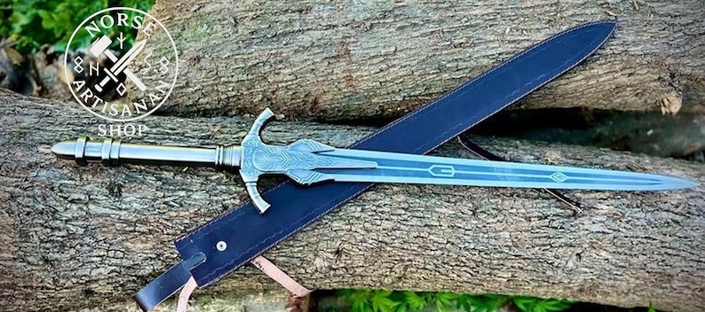 May include: A silver sword with a detailed hilt and a blue blade rests on a blue sheath. The sword is placed on a wooden surface. The image includes the text "Norse Artisans Shop" in a circular logo.