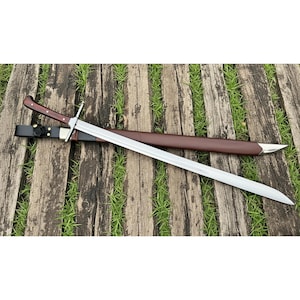 Può includere: Una lunga spada d'argento con un'impugnatura in legno marrone e un fodero in pelle. La spada è appoggiata su una superficie di legno con erba verde sullo sfondo. L'impugnatura ha una finitura marrone scuro.