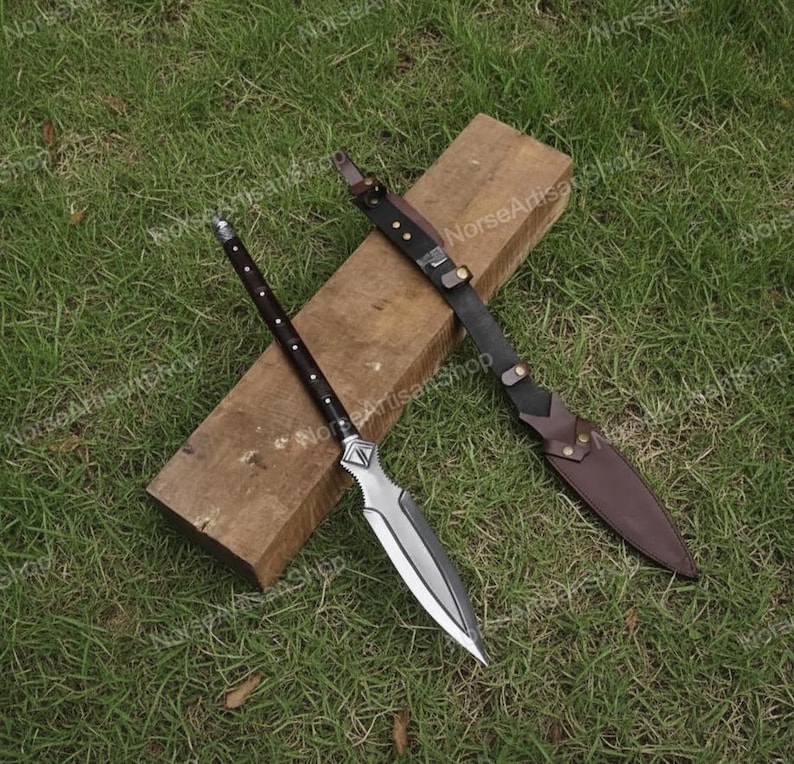 Puede incluir: Una lanza con una hoja plateada y un mango de madera oscura, apoyada sobre un bloque de madera. Tambi&eacute;n hay una funda y una correa de cuero. La lanza est&aacute; dise&ntilde;ada con una punta afilada y un mango decorativo.