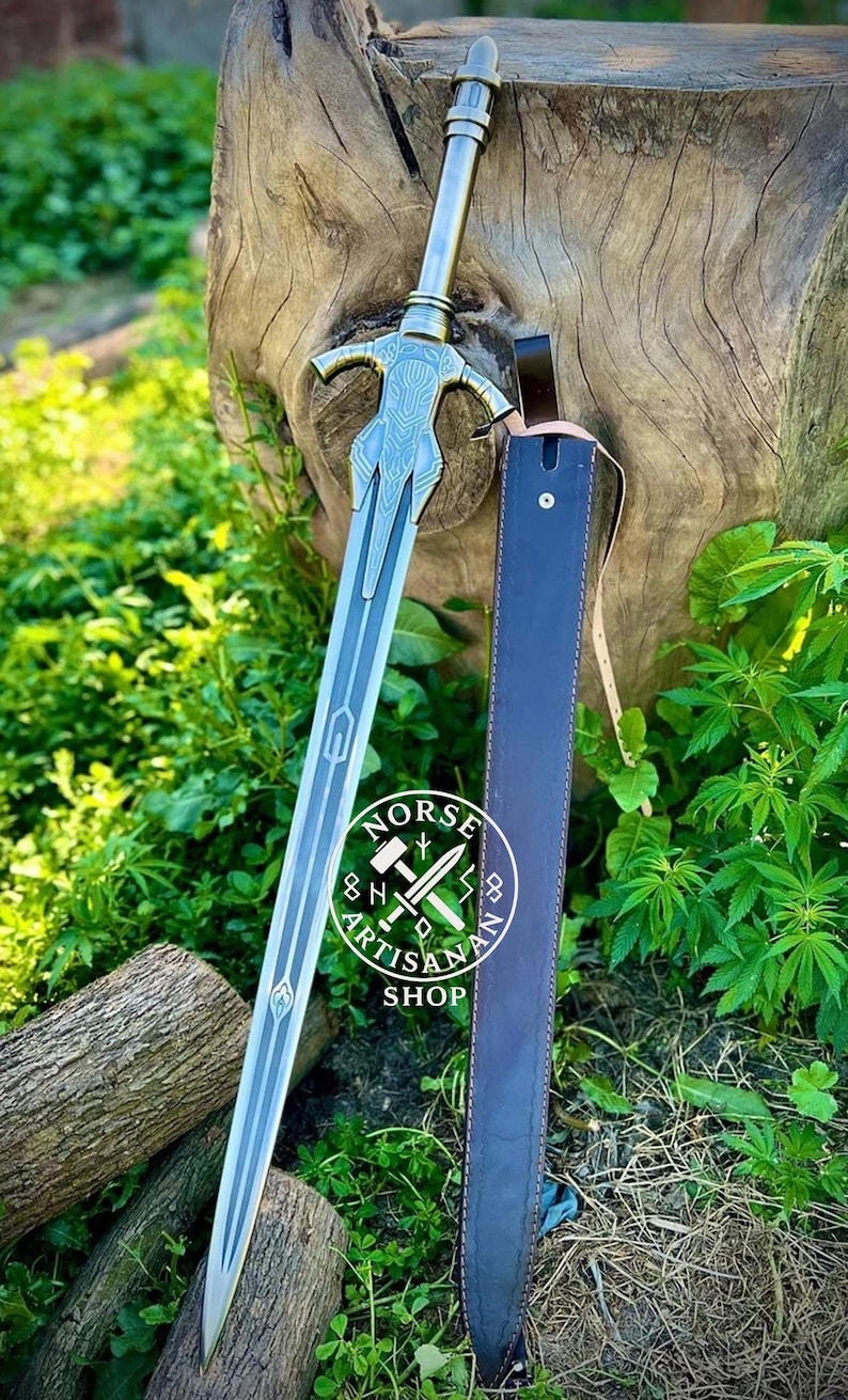 May include: A silver and blue sword with intricate designs, resting beside a dark blue leather sheath. The sword features a detailed hilt and blade, with the "Norse Artisan Shop" logo visible. The scene is set outdoors with green foliage.