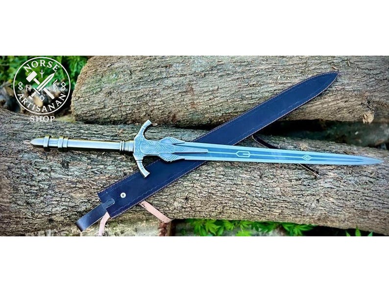 May include: A silver-colored sword with a decorative hilt and a long, light blue blade rests on a dark blue sheath. The sword is displayed on a bed of wooden logs. The logo for Norse Artisan Shop is visible in the upper left corner.