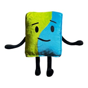 May include: A soft toy in the shape of a rectangle, split diagonally into lime green and blue sections. It features black arms, legs, and facial details, including two black eyes and a curved mouth. The toy has a cheerful expression.