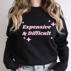 May include: Black sweatshirt with pink text that reads "Expensive & Difficult" with pink stars around the text.