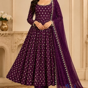 May include: A deep purple floor-length Anarkali dress featuring a repeating gold leaf pattern, long sleeves, and a round neckline. The outfit includes matching purple trousers and a sheer purple dupatta with a decorative beaded border trim.
