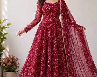 May include: A deep red floor-length dress with long sleeves and a round neckline, featuring a repeating white circular pattern throughout the fabric. The garment includes a matching sheer red dupatta draped over one shoulder with gold trim.