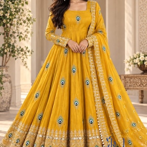 May include: A floor-length mustard yellow gown with long sleeves and a square neckline. The dress features embroidered peacock feather motifs throughout, with a wide, heavily embellished gold border at the hem and a matching yellow dupatta.