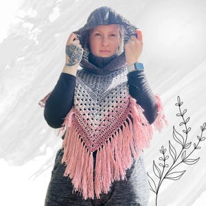 Könnte beinhalten: Ein handgefertigter Häkelponcho mit Kapuze. Der Poncho hat ein Grau- und Rosa-Verlaufsdesign mit langen rosa Fransen. Die Kapuze und der Rollkragen sind grau. Der Poncho ist als Schal oder Wickel konzipiert.