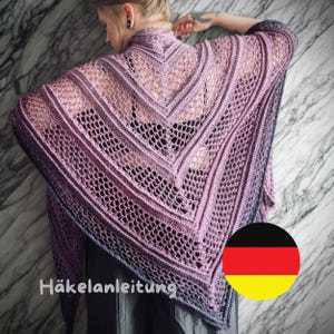 Könnte beinhalten: Ein handgefertigter, offen gewebter Schal in Lavendel- und Lilatönen. Der Schal hat ein zartes, spitzenartiges Muster mit V-Ausschnitt. Der Text "Häkelanleitung" ist unten links sichtbar. Der Schal ist über die Schultern einer Person drapiert.