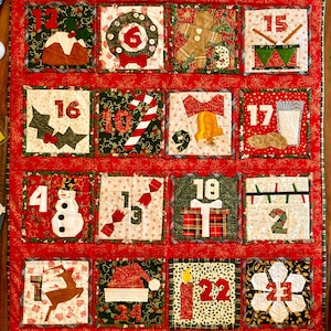 May include: A festive, handmade Christmas advent calendar. Each of the 24 squares features a unique Christmas-themed design and a number. The squares are predominantly red, green, and white, with images of festive ornaments and symbols. A seasonal decoration.