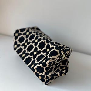 Op de afbeelding: Zwarte en crèmekleurige geometrische patroon etui met een gouden rits. De etui is gemaakt van een zachte, getextureerde stof. Het geometrische patroon is een herhalend stervormig ontwerp.