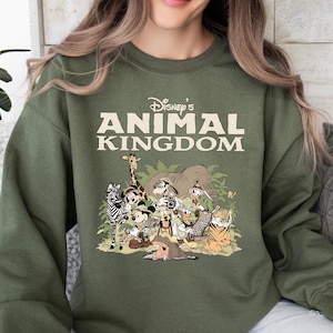 May include: An olive green sweatshirt with the text "Disney's Animal Kingdom" and a graphic of cartoon animals. The graphic includes a giraffe, zebra, elephant, and tiger. The sweatshirt has long sleeves and a crew neck, perfect for casual wear.