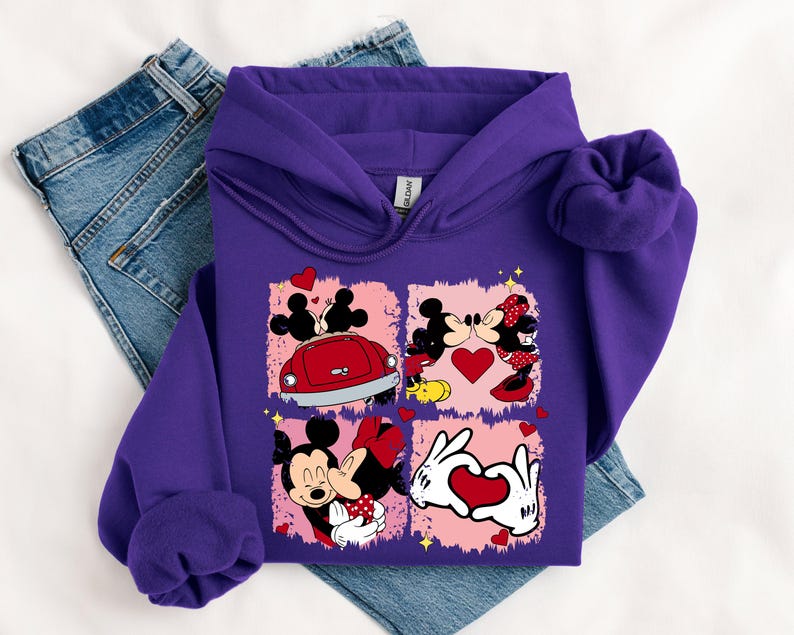 May include: A purple hoodie with a graphic of Mickey and Minnie Mouse in four romantic scenes. The design includes a red car, hearts, and the couple kissing. The hoodie is folded on top of a pair of blue jeans.