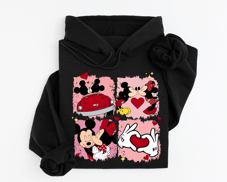 May include: Black hoodie with a vibrant graphic of Mickey and Minnie Mouse in romantic scenes. The design incorporates hearts, a red car, and a heart-shaped hand gesture, set against a pink backdrop.