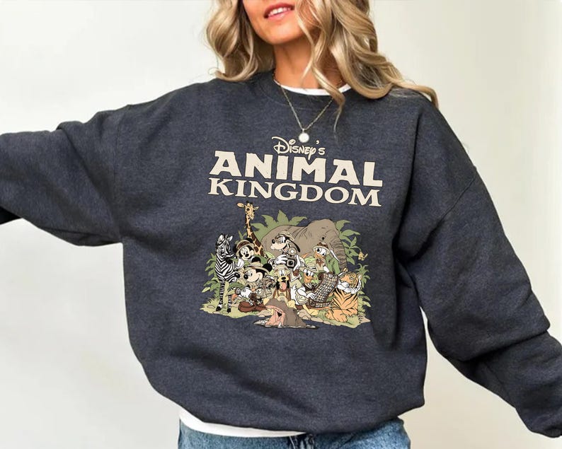 May include: Charcoal grey sweatshirt with the text "Disney's Animal Kingdom" in cream. The graphic depicts cartoon animals including a zebra, giraffe, and tiger, set against green foliage. A casual, comfortable top.