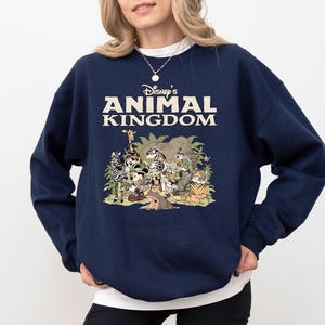 May include: A navy blue crew neck sweatshirt with the text "Disney's Animal Kingdom" in cream. The graphic depicts cartoon animals including a zebra, giraffe, and tiger. The sweatshirt is a casual style.