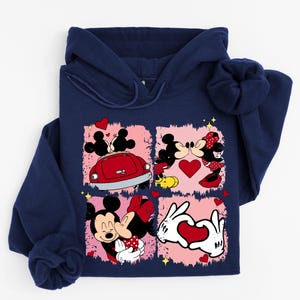 May include: Navy blue hoodie with a graphic of Mickey and Minnie Mouse in romantic scenes. The design includes hearts, a red car, and a heart-shaped hand gesture, set against a pink background.