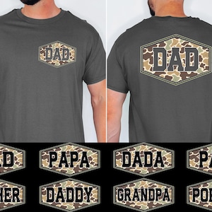 May include: Dark gray t-shirt with a camouflage "DAD" design on the front and back. The design is in a hexagonal shape. Additional designs include "PAPA", "DADA", "PAPI", "FATHER", "DADDY", "GRANDPA", and "POPPOP".