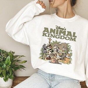 May include: White sweatshirt with a green graphic of cartoon animals, such as a giraffe and zebra. The text "Disney's Animal Kingdom" is printed above the animal illustration in green.