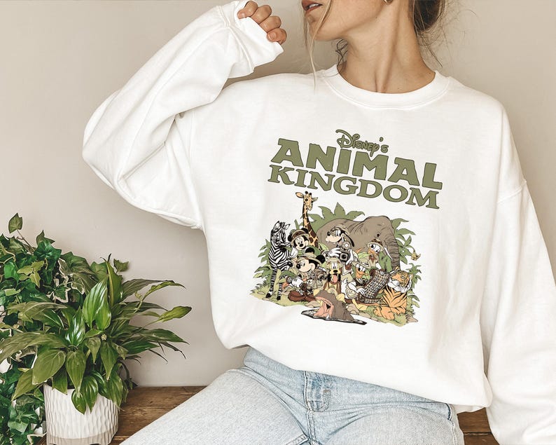 May include: White sweatshirt with a green graphic of cartoon animals, such as a giraffe and zebra. The text "Disney's Animal Kingdom" is printed above the animal illustration in green.