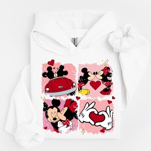 May include: White hoodie with a four-panel design featuring Mickey and Minnie Mouse. The panels show the couple in romantic poses, with hearts and a red car. The design includes a heart-shaped hand gesture.